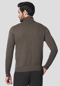 Brązowy sweter z dzianiny z wysokim kołnierzem, prążkowanymi mankietami i dołem. Tekstura wydaje się gładka i miękka, a fason jest dopasowany.