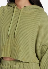Groene geribbelde cropped hoodie met een trekkoordcapuchon, textuurstof en een relaxte pasvorm. Opvallende goudkleurige hardware bij de trekkoorden.