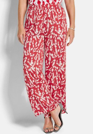 Donna che indossa pantaloni a gamba larga con motivo rosso e bianco e vita elastica, abbinati a sandali con tacco alto argentati e scintillanti.