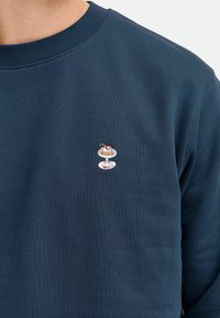 Sweatshirt bleumarin cu un guler rotund cu nervuri și un mic design cu desert brodat pe partea stângă a pieptului. Material moale, texturat.