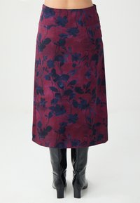 Bordeauxroter Rock mit Blumenmuster und dunkelblauen Blumen, knielang, mit glatter Textur und tailliertem Bund. Kombiniert mit schwarzen kniehohen Stiefeln.