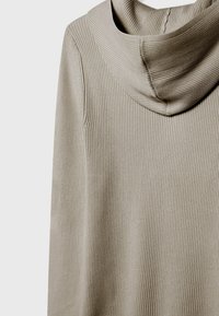 Tela beige acanalada con una capucha suave y caída. El diseño presenta una superficie texturizada y una silueta relajada con líneas verticales.