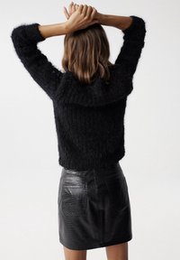 Hedvábný černý svetr s kulatým výstřihem a přiléhavým střihem v kombinaci s lesklou černou mini sukní z faux kůže s krokodýlí texturou.