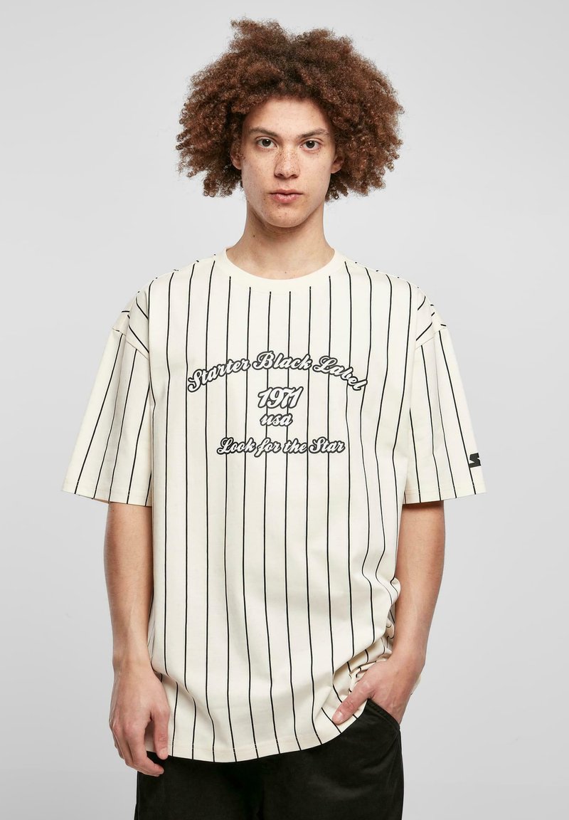 Kortærmet, cremefarvet T-shirt med sorte lodrette striber. Har en oversized pasform og trykt tekst i kontrastfarver på forsiden.