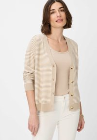 Beiger gestrickter Cardigan mit horizontalen Streifen, mit V-Ausschnitt, Knopfleiste und gerippten Bündchen. Getragen über einem beigen Top.