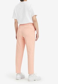 Rosa byxor med smal passform, utrustad med två bakfickor och en slät yta, kombinerat med en vit kortärmad topp och vita sneakers.