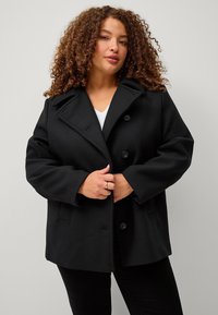 Cappotto in misto lana nero con colletto a batt collare, design doppiopetto e grandi bottoni. Presenta una vestibilità comoda e tasche laterali.
