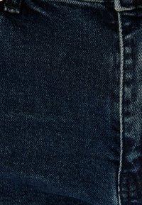 Tela de mezclilla azul oscuro con una textura suave, con costuras prominentes a lo largo de las costuras y un corte típico de vaqueros.