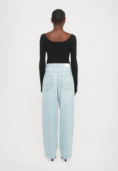 Body a maniche lunghe nera abbinato a jeans a gamba larga azzurri chiari, con vita alta e cinque tasche. Dettaglio bianco sulla vita.