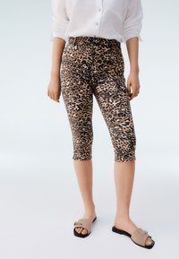 Legginsy capri w panterkę o dopasowanym kroju, z wysokim stanem. Materiał ma gładką fakturę, łącząc beżowy i czarny kolor.