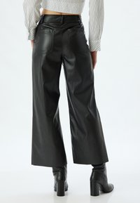 Zwarte faux leren wijde broek met twee achterzakken, een gladde textuur en een hoge taille ontwerp. Gestyled met zwarte haklaarzen.