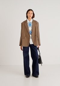 Καφέ υπερμεγέθη σακάκι, μπλε πουλόβερ argyle πάνω από λευκό πουκάμισο, τζιν με φαρδιά πόδια σκούρου χρώματος και μαύρα παπούτσια. Κρατά μια μαύρη τσάντα χειρός.