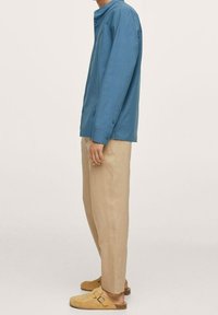 Camicia azzurra a maniche lunghe con colletto a band, pantaloni beige su misura e sandali color nocciola. L'outfit ha una vestibilità rilassata e una consistenza liscia.