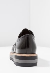 Chaussure en cuir verni noir avec des détails de brogue, semelle texturée et un intermédiaire en liège contrastant.  Bout rond, design à talon bas.