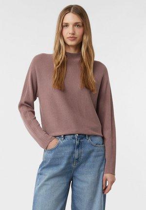 Różowy sweter z dzianiny z wysokim kołnierzem i prążkowanymi rękawami, w zestawieniu z jasnoniebieskimi, luźnymi dżinsami.