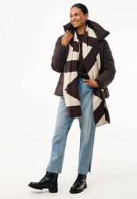 Brun puffjacka, krämfärgad och brun mönstrad scarf, mörk tröja, ljusblå jeans, svarta snörade stövlar med strukturerad yta.