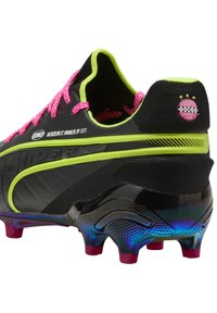 Scarpe da calcio nere con lacci rosa, accenti verde neon e una suola lucida a fantasia. Presentano una tomaia testurizzata e il logo del club sul tallone.