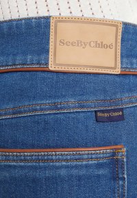 Vaqueros de mezclilla de color azul claro, con una etiqueta de cuero marrón marcada "SeeByChloé" y costuras en contraste en el bolsillo trasero.