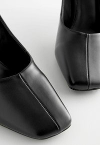 Czarne skórzane buty o kwadratowym nosku, gładkiej fakturze i kontrastującym przeszyciu. Minimalistyczny kształt, elegancki wygląd.