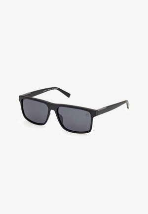 Gafas de sol rectangulares negras con lentes oscuros. La montura es mate, hecha de plástico, y presenta acentos plateados en las patillas.