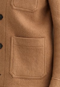 Bruine, gefilte wol jacket met knoopsluiting en twee opgestikte zakken met hoekige details. Zachte textuur en warme tint.