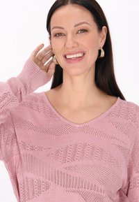 Pulover tricotat de culoare roz deschis, cu decolteu în V, model texturat cu țesături deschise și mâneci lungi cu tiv din jerseu.