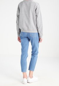Grijze katoenen sweatshirt, blauwe denim, cropped fit, achteraanzicht, witte sneakers, zichtbare stiksels op de spijkerbroek, minimalistisch design.