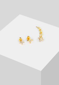Ein Set aus goldenen Ohrringen, bestehend aus zwei sternförmigen Steckerohrringen mit Kristallen und einem geschwungenen Ohrhänger mit mehreren Sternelementen, alles in glänzendem Finish.