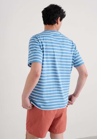 Randig t-shirt i ljusblå och vit bomull, med korta ärmar och rund halsringning. Kombinerad med korallfärgade shorts.