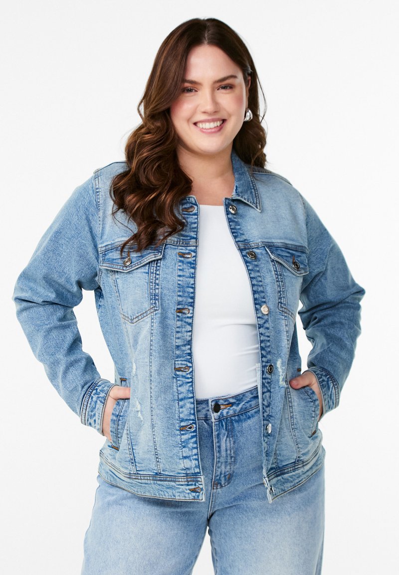 Šviesiai mėlynas džinsinis švarkas su apykakle, priekinėmis kišenėmis ir mygtukų uždarymu. Turi šiek tiek tekstūruotą paviršių ir laisvą kirpimą.