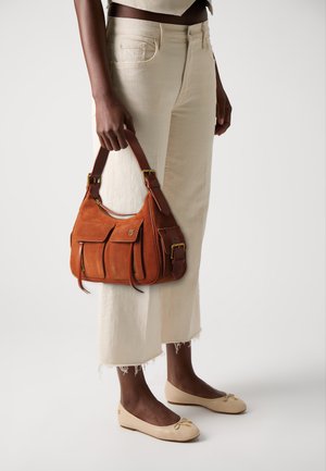 Brown suede handbag with two front pockets, structured design, and dual straps. Worn with cream cropped pants and beige flats.