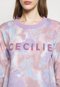 Felpa in cotone con un pattern tie-dye pastello in toni di rosa e blu, con scritte testurizzate di colore viola che formano la parola "CECILIE" sulla parte frontale.