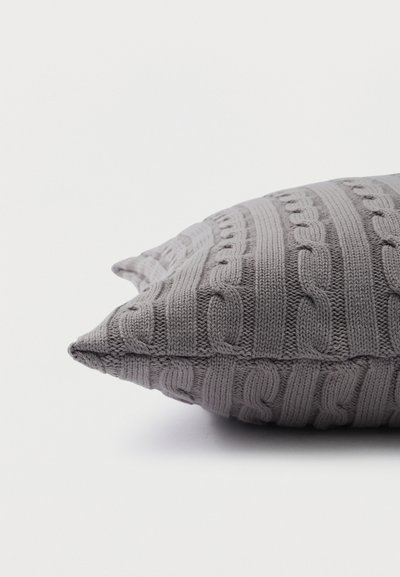 Γκρι πλεκτό μαξιλάρι με σχέδιο καλωδίου ξαπλωμένο επίπεδα σε λευκή επιφάνεια.