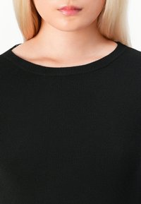 Svart ribbestrikket topp med rund halslinning, som har et teksturert stoff som gir en tettsittende passform og jevn overflate over torsoen.