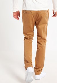 Bruna chinos med smal passform och bakfickor, parat med vita skor. Slät tyg, skräddarsydd design och minimalistiska detaljer.