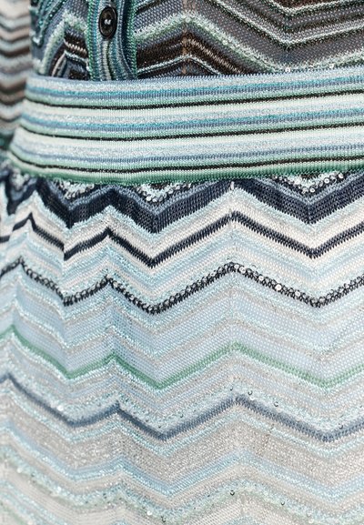 Pleteni kroj s šivanim vzorcem v odtenkih modre, zelene in črne barve, z metalnimi nitmi in teksturiranimi poudarki na tkanini.