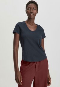 Maglietta a maniche corte blu navy con scollo a barca, realizzata in morbido cotone. Caratterizzata da una vestibilità rilassata e una consistenza liscia. Abbinata a pantaloni bordeaux.