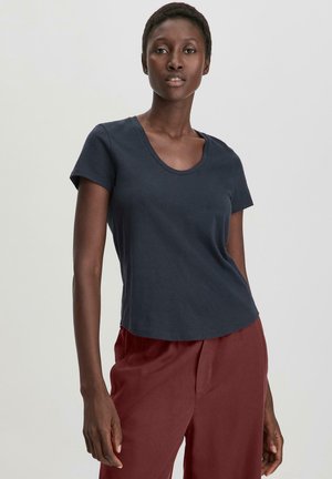 Camiseta de manga corta azul marino con escote redondeado, hecha de algodón suave. Presenta un ajuste relajado y una textura suave. Combinada con pantalones burdeos.