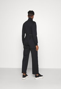 Černý overal s dlouhými rukávy a vysokým límcem, stažený v pase opaskem. Nosit s černými teniskami, s volnějším střihem.