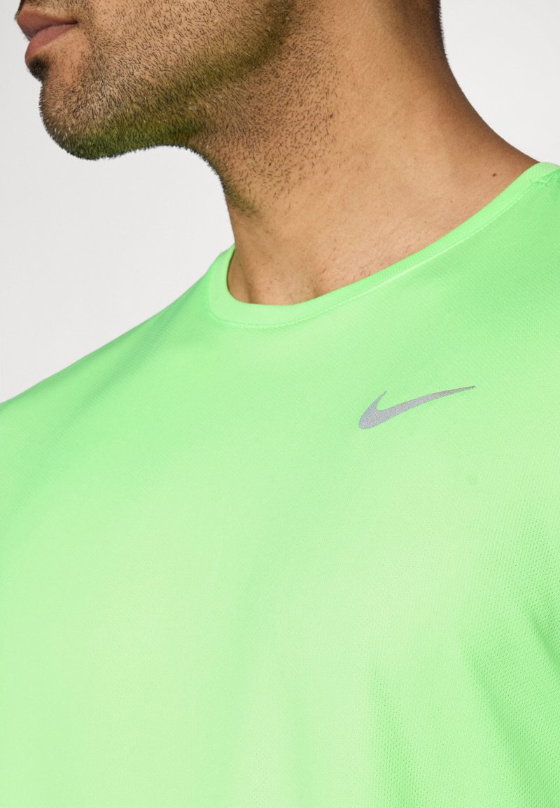 Neongrünes Sport-T-Shirt mit rundem Ausschnitt und kurzen Ärmeln. Mit einem kleinen silbernen Nike-Logo oben links. Weicher, strukturierter Stoff.