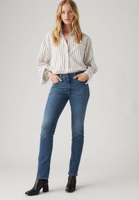 White striped button-up shirt with rolled sleeves, paired with form-fitting dark blue jeans and black heeled ankle boots.
