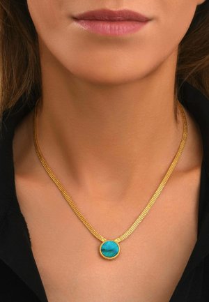 Collier chaîne en or avec un pendentif turquoise rond porté autour du cou d'une femme au-dessus d'un haut noir.
