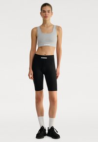 Grijze crop top met logo, gecombineerd met zwarte bike shorts met logo. Beide zijn gemaakt van rekbare materialen voor actieve kleding.