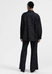 Camicia di jeans blu e pantaloni a campana con decorazioni floreali nere. L'outfit ha una vestibilità comoda con maniche lunghe e colletto.