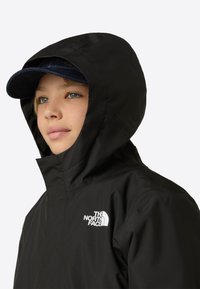 Crna vodootporna jakna s kapuljačom i visokim ovratnikom. The North Face logo u bijeloj boji na lijevoj strani prsnog dijela. Mekana tekstura, aerodinamičan dizajn.