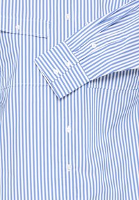 Light blue and white striped dress shirt, featuring a button-down front, a pocket on the left chest, and long sleeves. Smooth cotton fabric.
