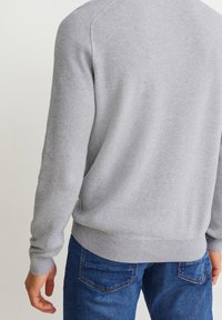 Szary sweter z prążkowanej dzianiny z długimi rękawami, okrągłym dekoltem i dopasowanym obszyciem. Połączony z niebieskimi dżinsami, podkreślając kontrast tekstur i materiałów.