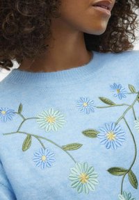 Light blue knitted sweater featuring floral embroidery in blue, green, and yellow with leaf accents, round neckline, and textured fabric.
