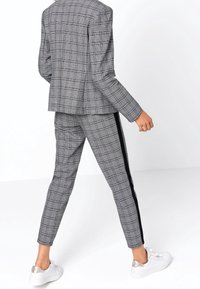 Šedý kostkovaný blejzr s odpovídajícími kalhotami, který má slim fit, boční pruhy a bílé tenisky. Texturovaná tkanina s propracovaným designem.