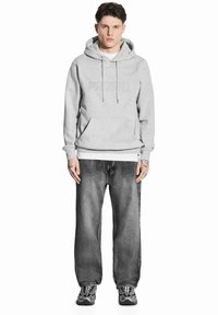 Szara bluza z kapturem i kieszenią kangurką, w połączeniu z wyblakłymi czarnymi dżinsami. Czarno-szare sneakersy z wyraźnym wzorem na podeszwie.